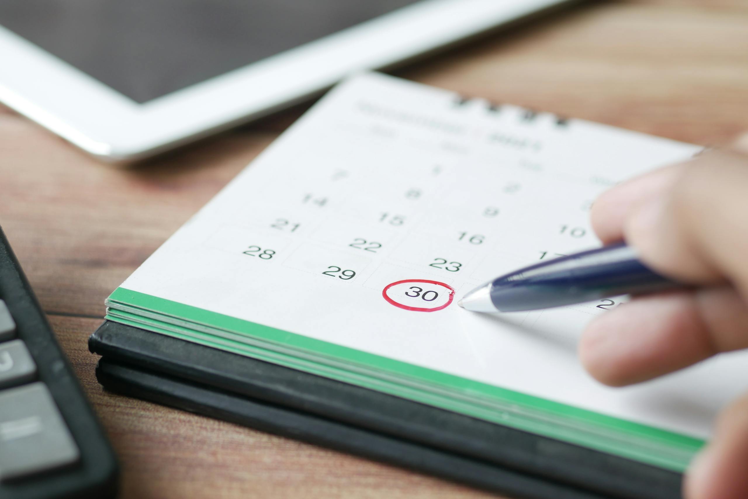 Close-up shot of a hand marking a date on a calendar with a pen, emphasizing planning and scheduling.